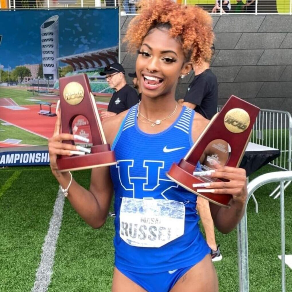 Smiling athlete in blue holding two NCAA trophies